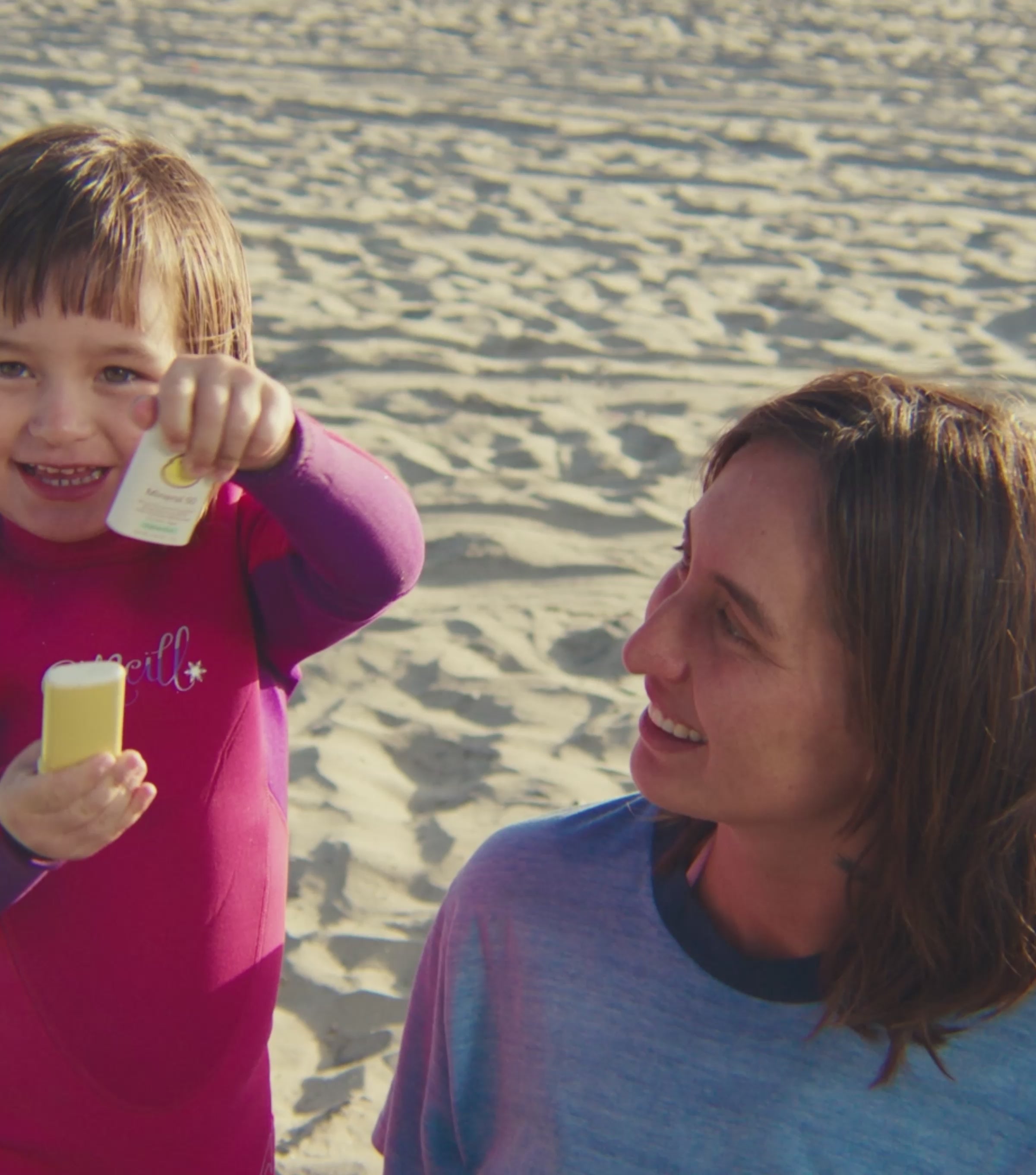 Little girl putting sunscreen on her mom at the beach