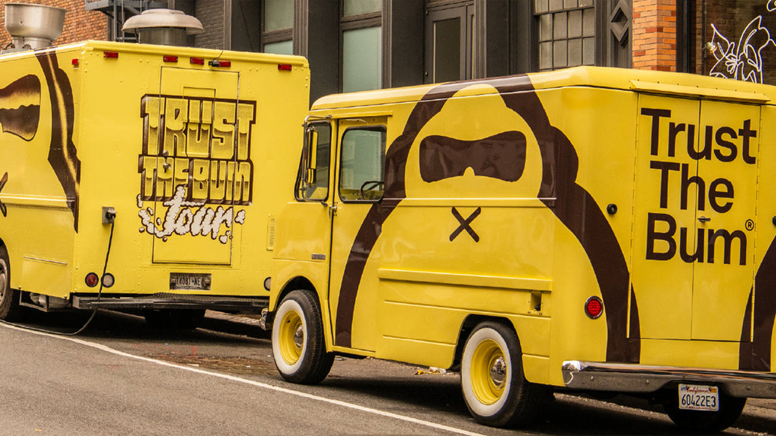 Two yellow food trucks with Trust the Bum branding on a street.
