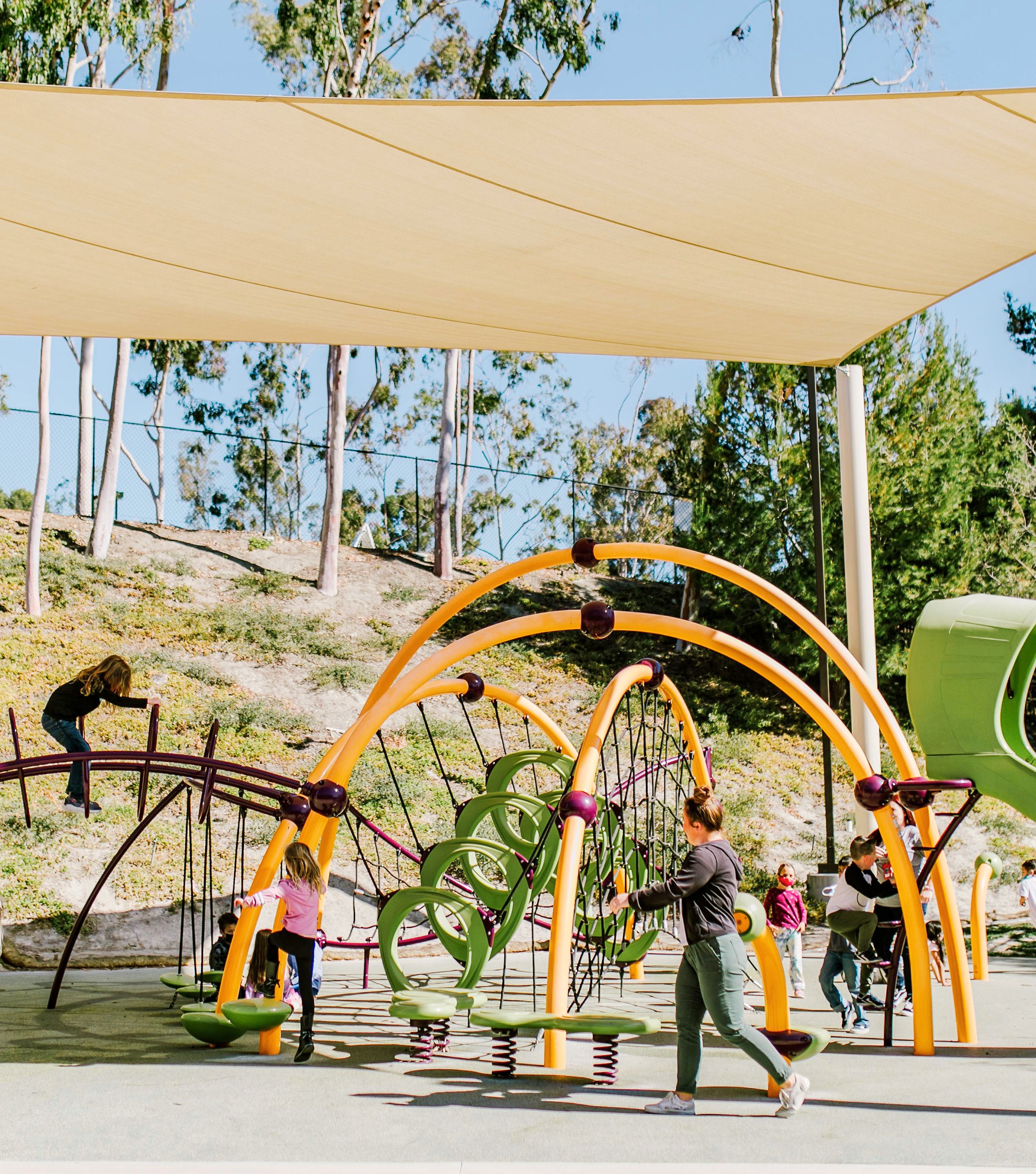 Kids and parents enjoying a shaded playground with modern equipment, highlighting PTG Sun Education Collection - Sun Bum.